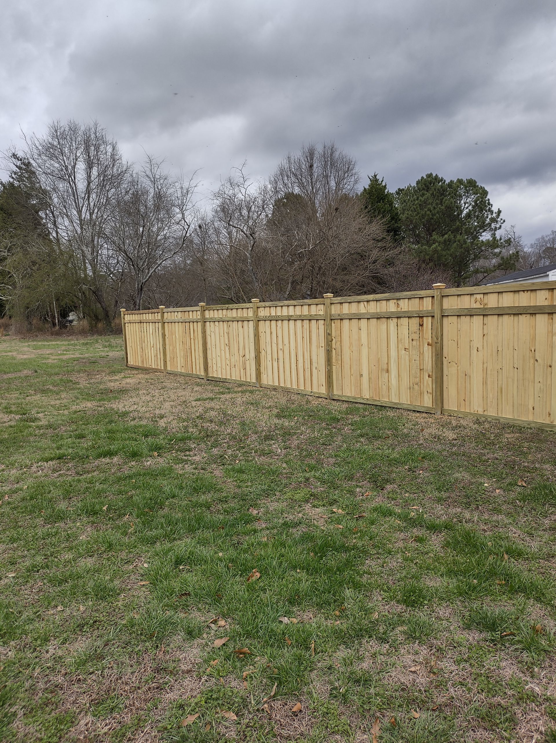 Wooden privacy fence along a grassy field under a cloudy sky