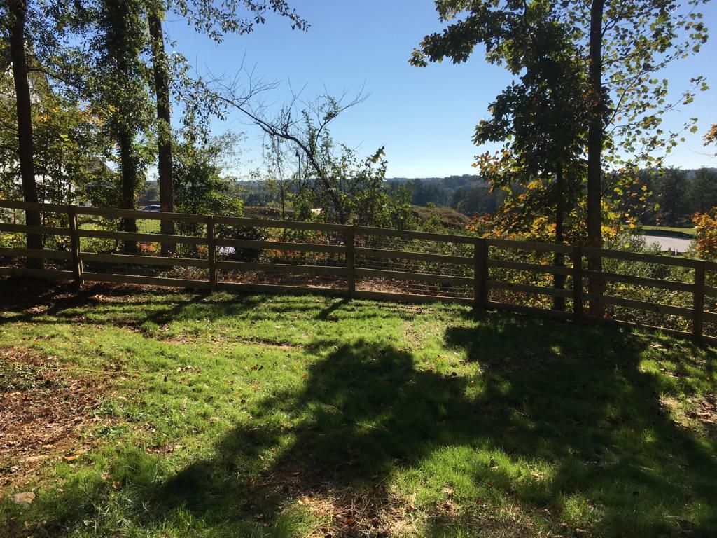 Sunlit grassy yard with wooden fence and trees overlooking a distant landscape