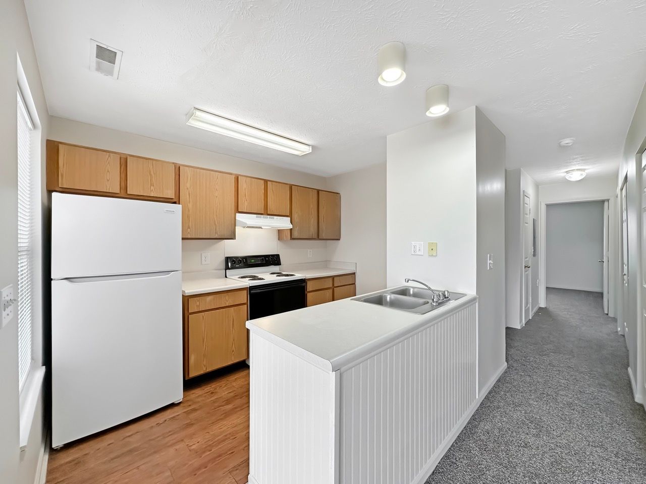 A kitchen with a refrigerator , stove , sink and wooden cabinets.