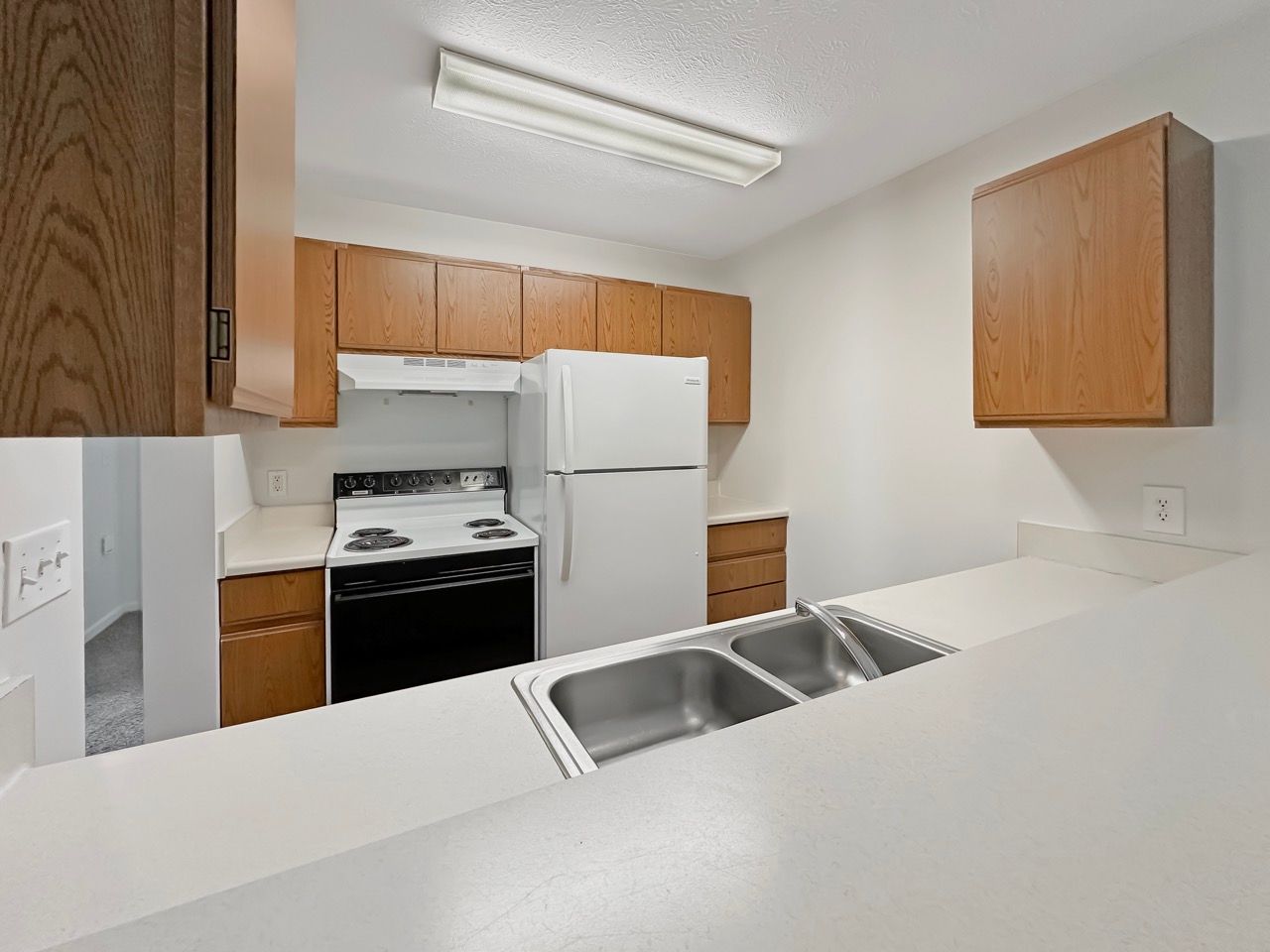 A kitchen with a stove , refrigerator , sink and wooden cabinets.