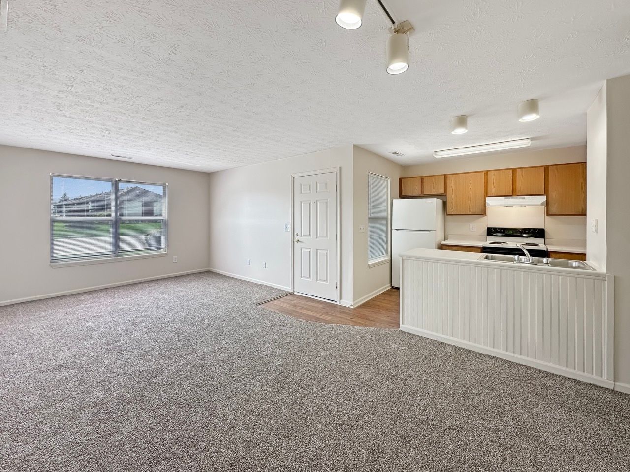 An empty living room with a kitchen in the background.