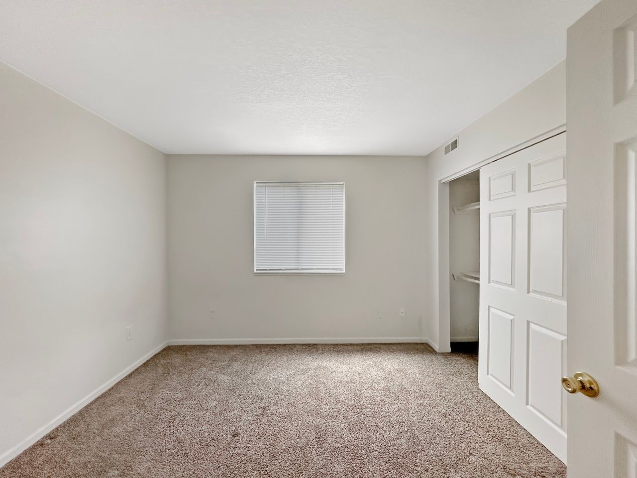 An empty bedroom with a window and a closet.