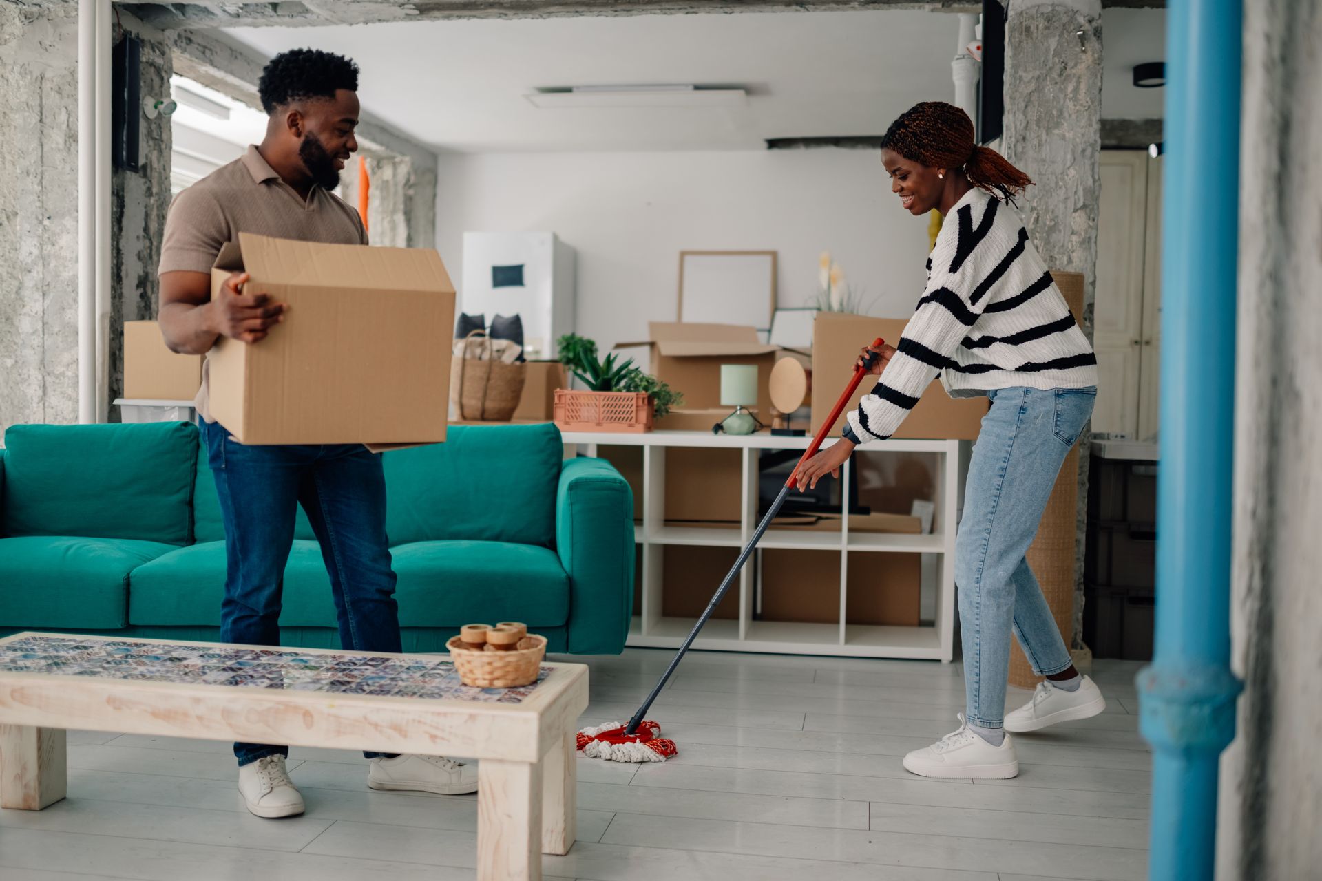 Man holding a box, woman sweeping floor; couple moving into a new apartment.