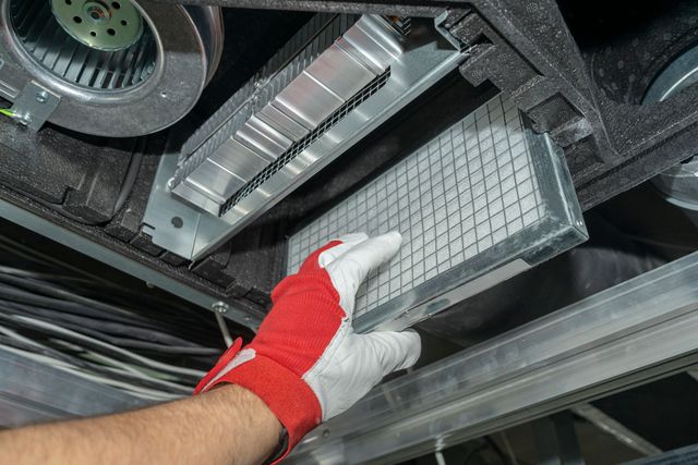 Gloved hand removing a rectangular air filter from a vehicle’s undercarriage compartment