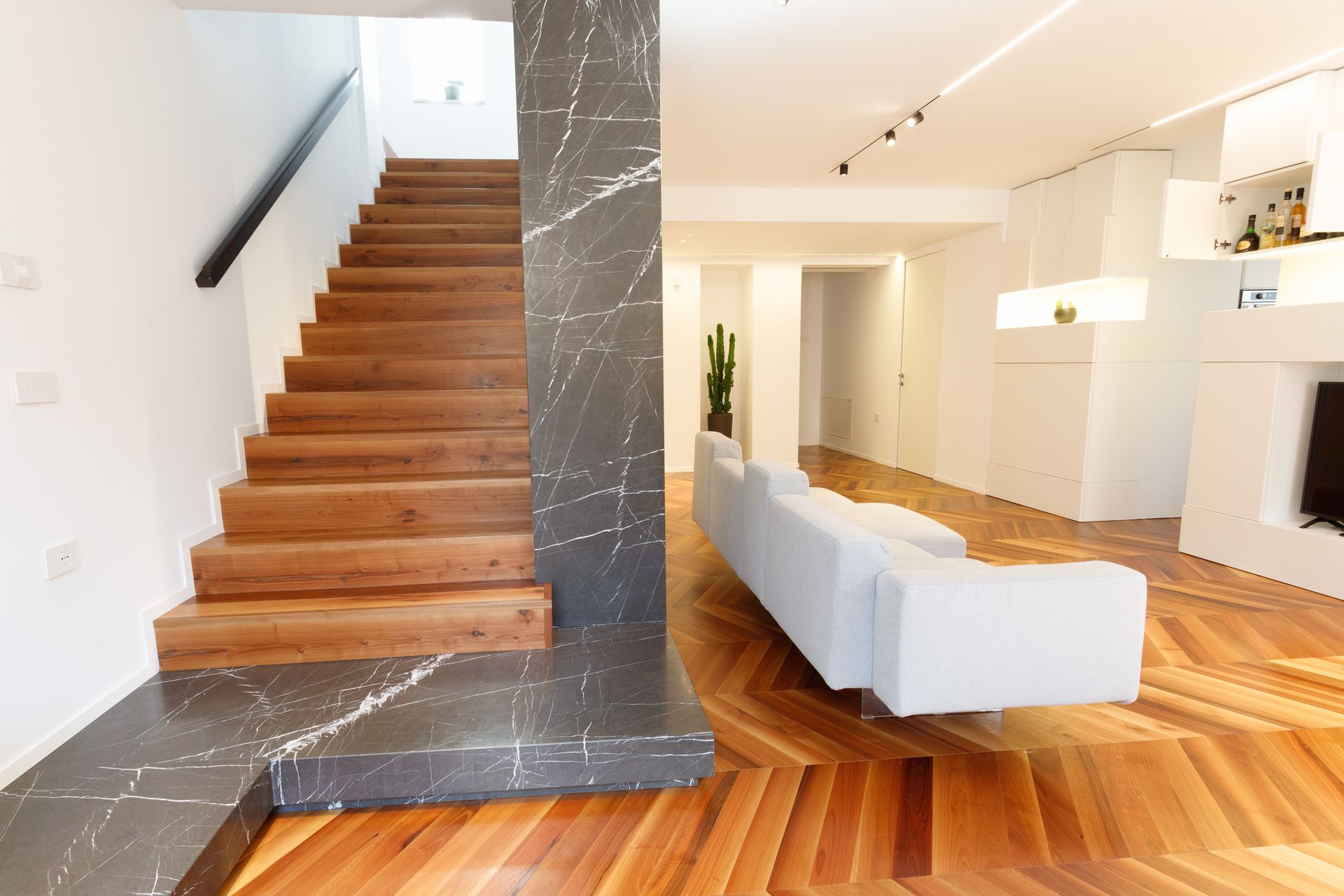Interni moderni a pianta aperta con scala in legno, colonna grigia e pavimento in parquet chiaro a spina di pesce.
