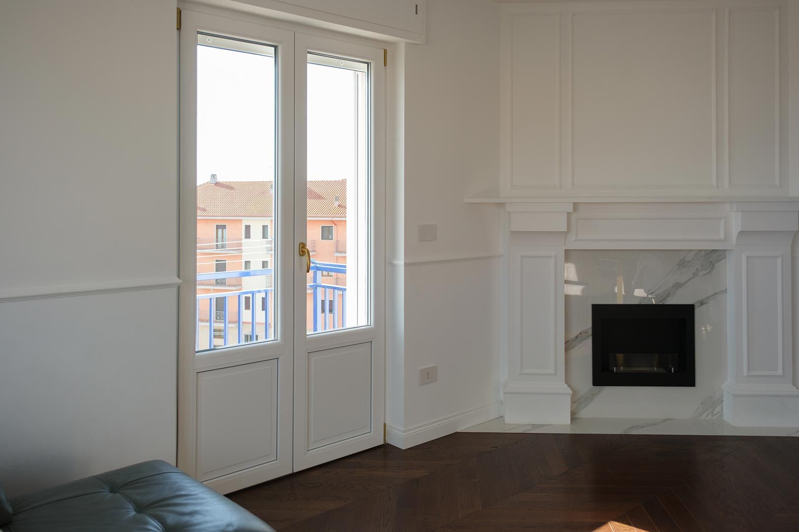 Luminoso soggiorno con camino bianco, pavimento in legno scuro e porte finestre che si affacciano sulla vista della città.