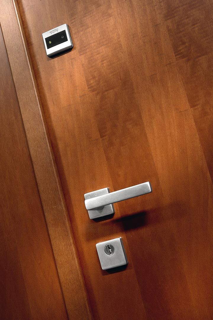 Porta in legno con maniglia argentata, serratura e piccola tastiera o sensore sopra di essa.