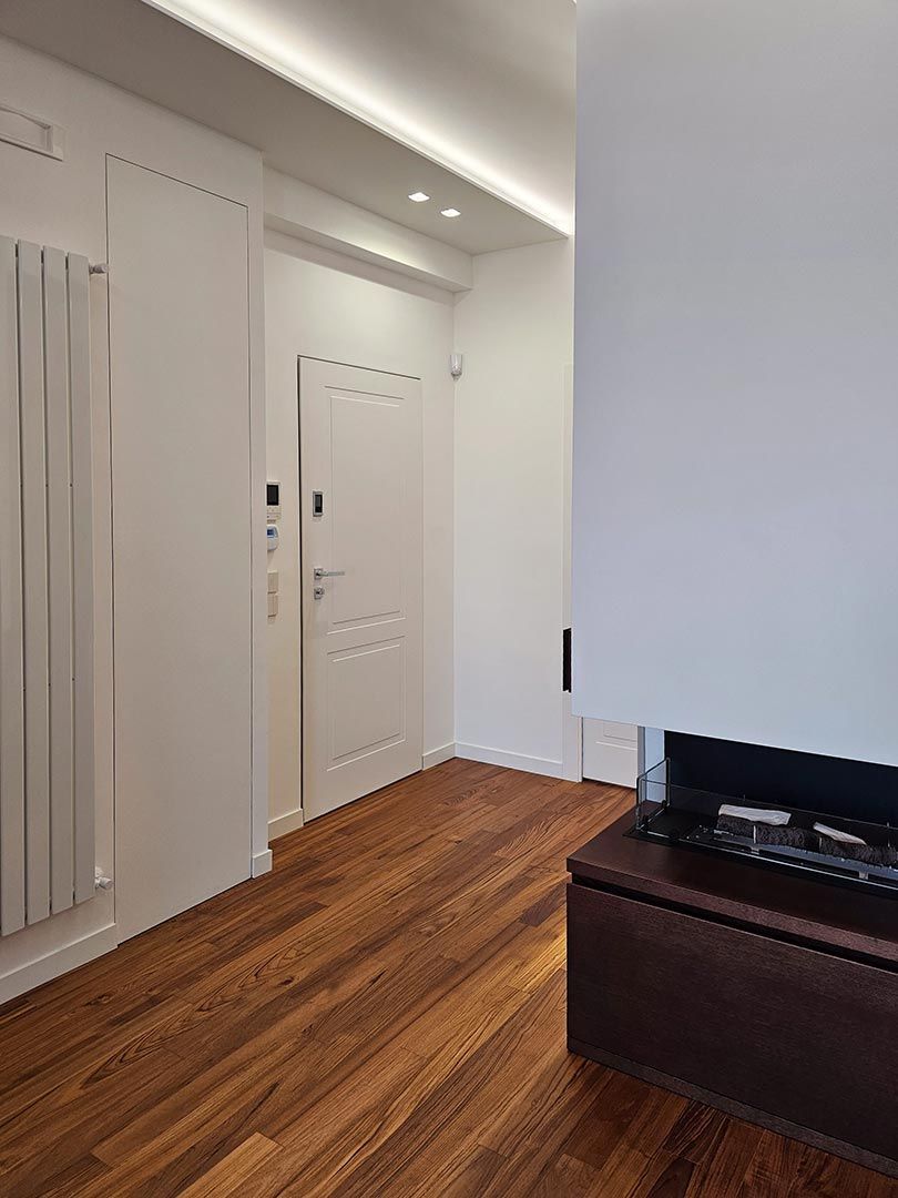 Luminoso corridoio con porte bianche, pavimento in legno e un mobile porta TV scuro in primo piano.