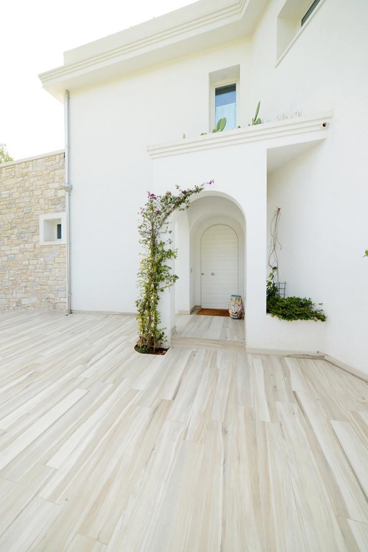Esterno della casa in stucco bianco con ingresso ad arco, portale ricoperto di rampicanti e cortile piastrellato di colore chiaro.