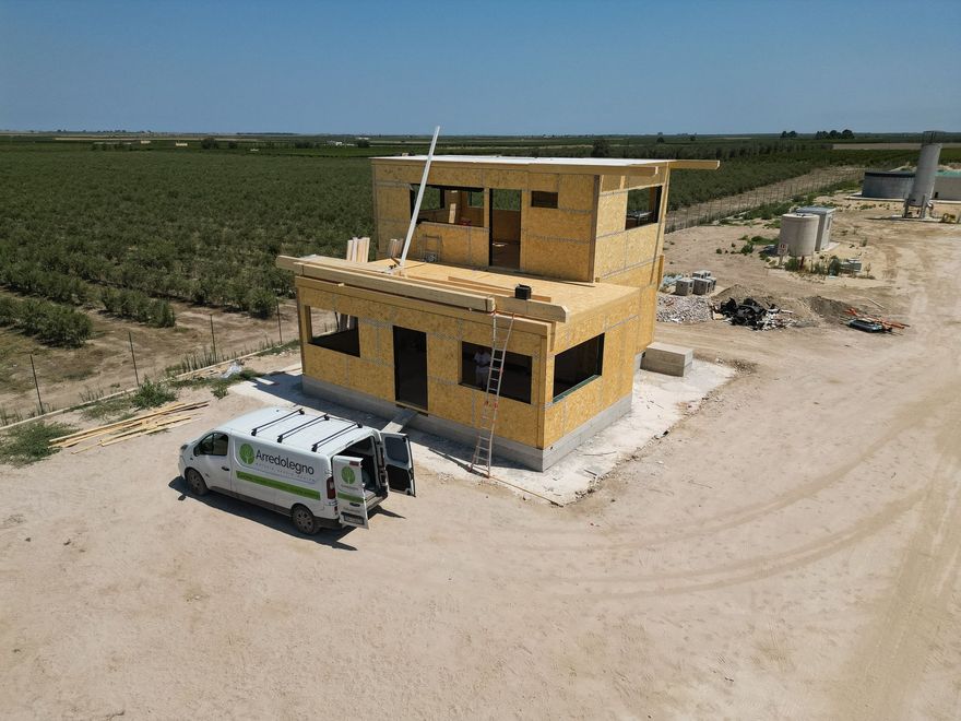 Casa moderna color beige con dettagli in legno, ampie finestre e giardino paesaggistico illuminato dalla luce naturale.