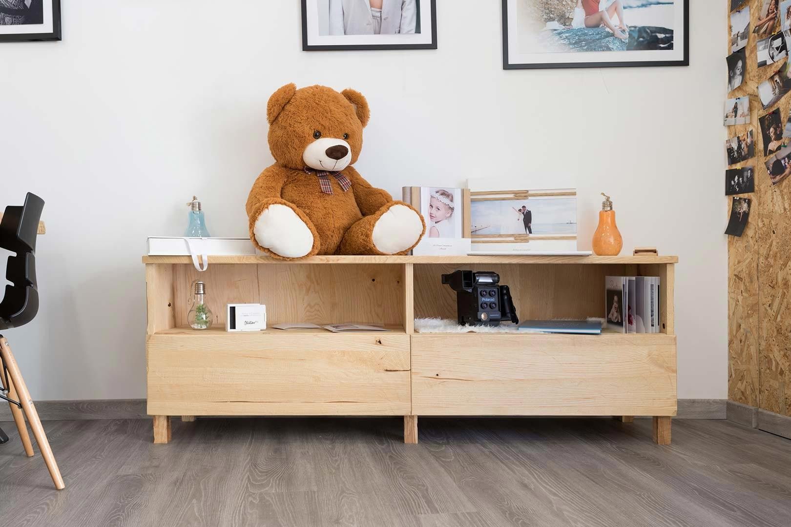 Un orsacchiotto marrone su una mensola di legno chiaro in una stanza minimalista, con quadri incorniciati alla parete.