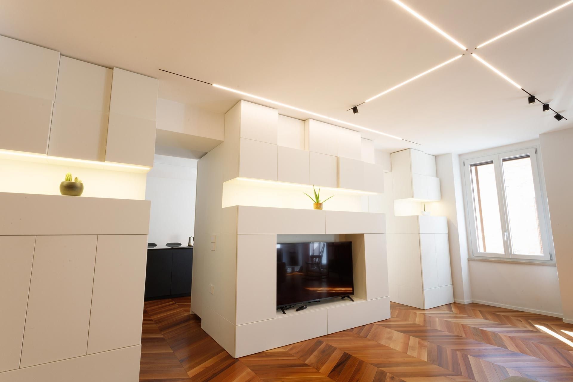 Soggiorno moderno bianco con camino integrato, pavimento in parquet a spina di pesce e ampie finestre.