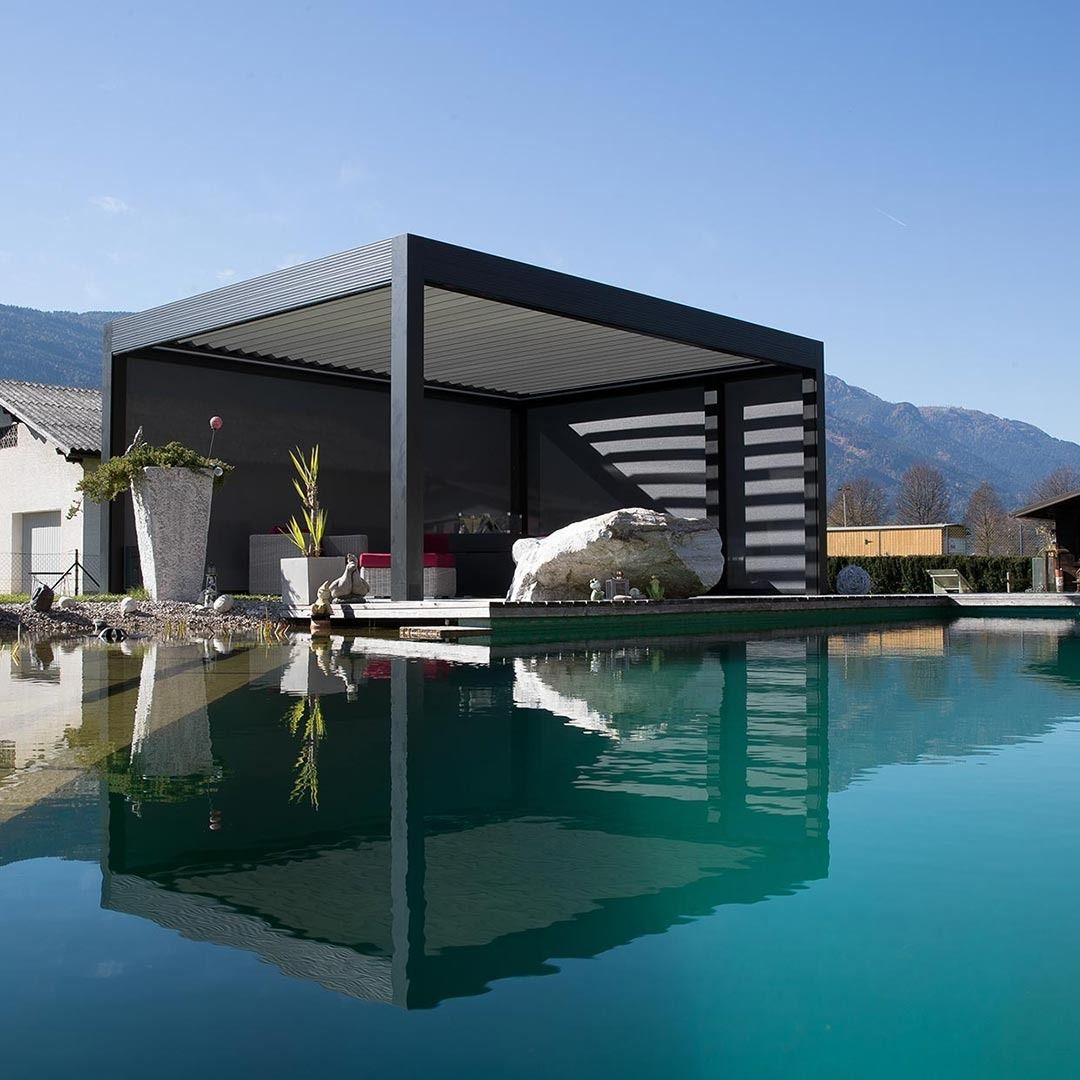Moderno padiglione nero a bordo piscina che si specchia nelle tranquille acque turchesi della vasca, con le montagne sullo sfondo.