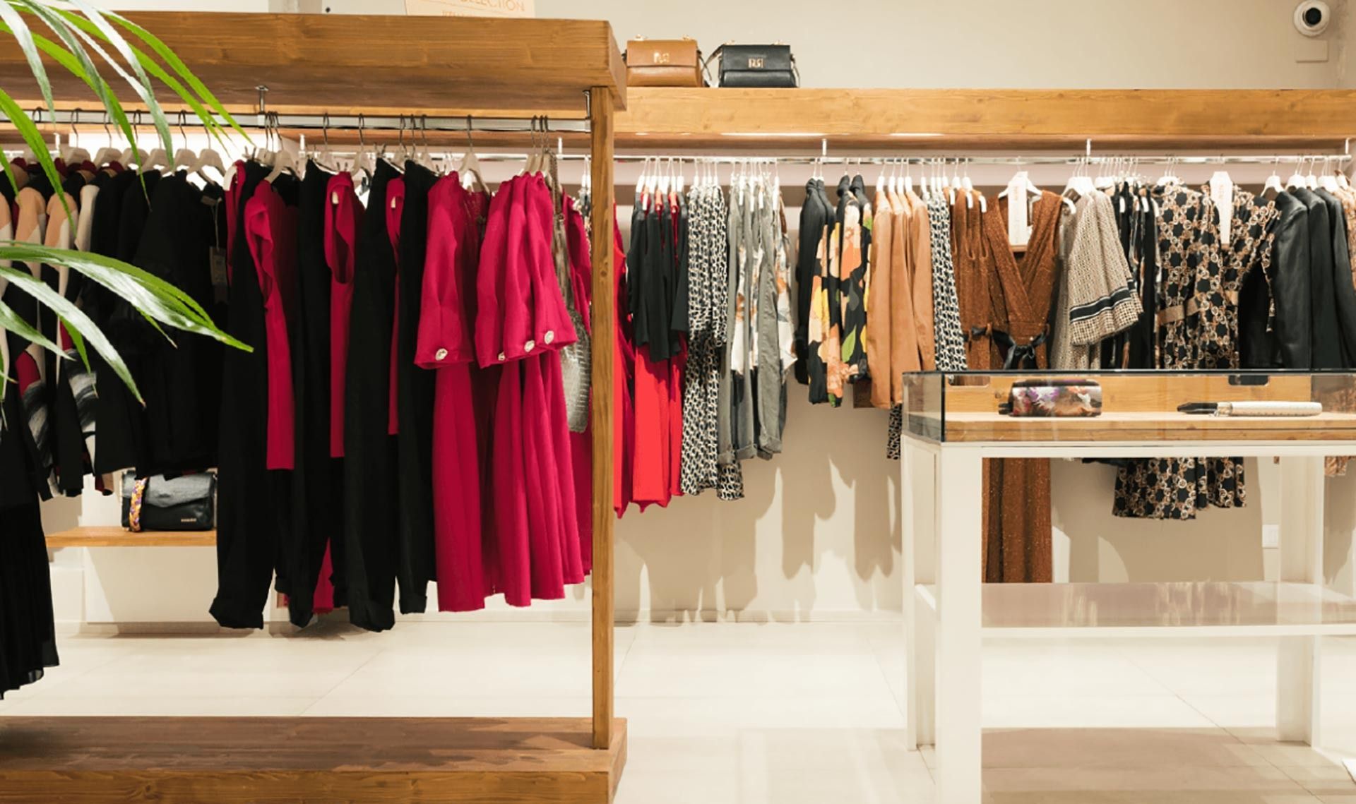 Boutique di abbigliamento con appendiabiti pieni di vestiti e top neri, rosa e beige in esposizione.