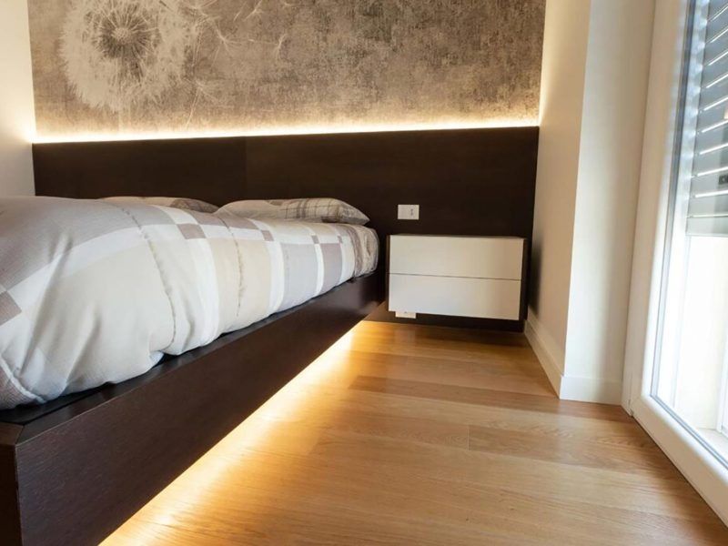 Camera da letto moderna con letto basso, pavimento in legno caldo, applique a parete e finestra con tende.