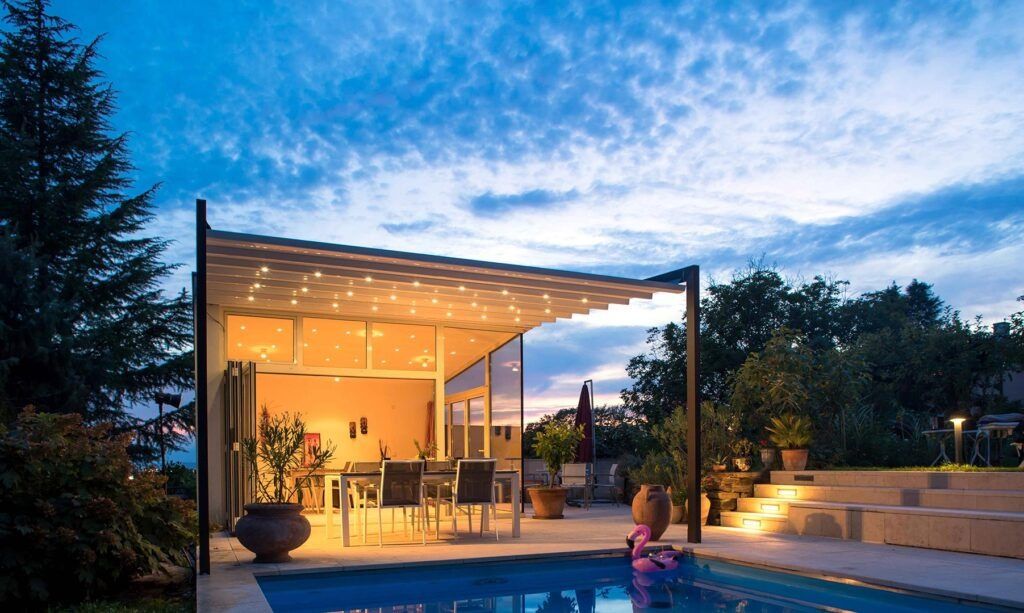 Casa moderna con patio illuminato da luci calde, pareti in vetro e piscina al crepuscolo