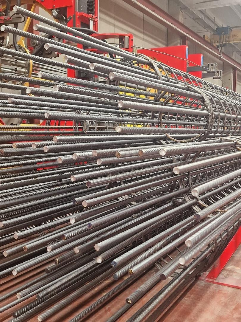 File di barre o tondini di metallo accatastati in un corridoio di un magazzino con scaffalature industriali rosse.
