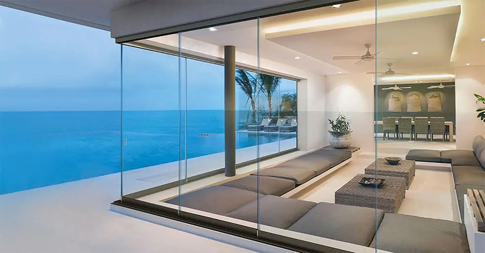 Moderno patio fronte oceano con pareti in vetro, comode sedute bianche e piscina con vista sul mare.