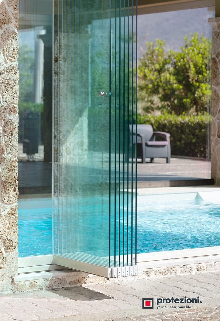 Pannello di vetro accanto a una piscina turchese con posti a sedere da patio e vegetazione sullo sfondo.