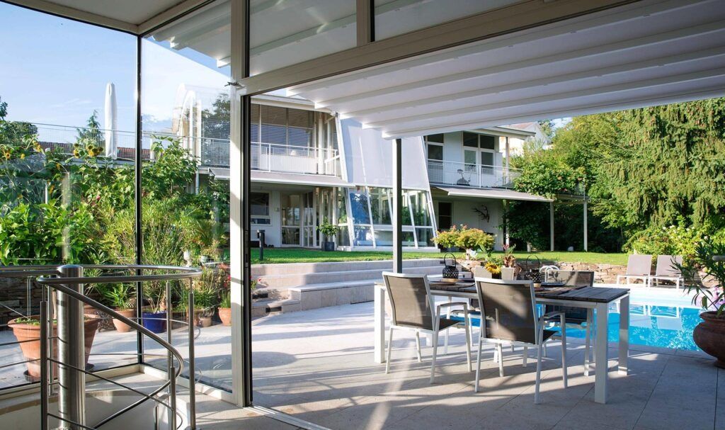 Patio moderno con sedie da pranzo, piscina e lussureggiante cortile in stile resort sotto una tettoia ombreggiata.