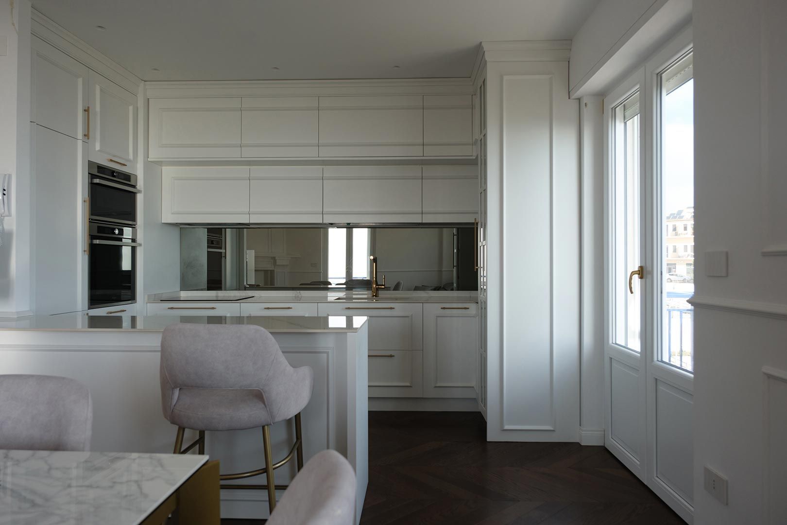 Cucina moderna e luminosa, di colore bianco, con isola in marmo, paraschizzi a specchio e ampie finestre.