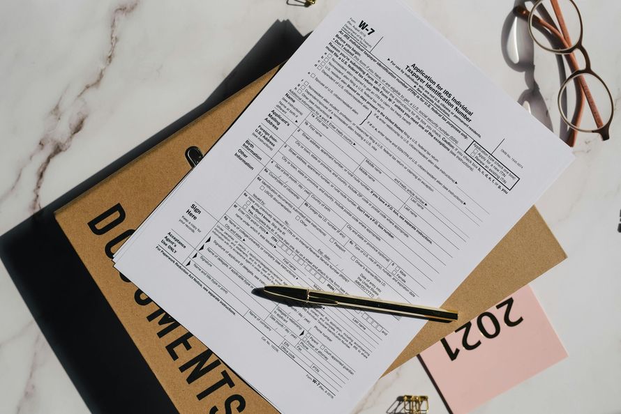 A top-down view of a document, a pen, eyeglasses, and a 2021 label resting on a white marble surface.