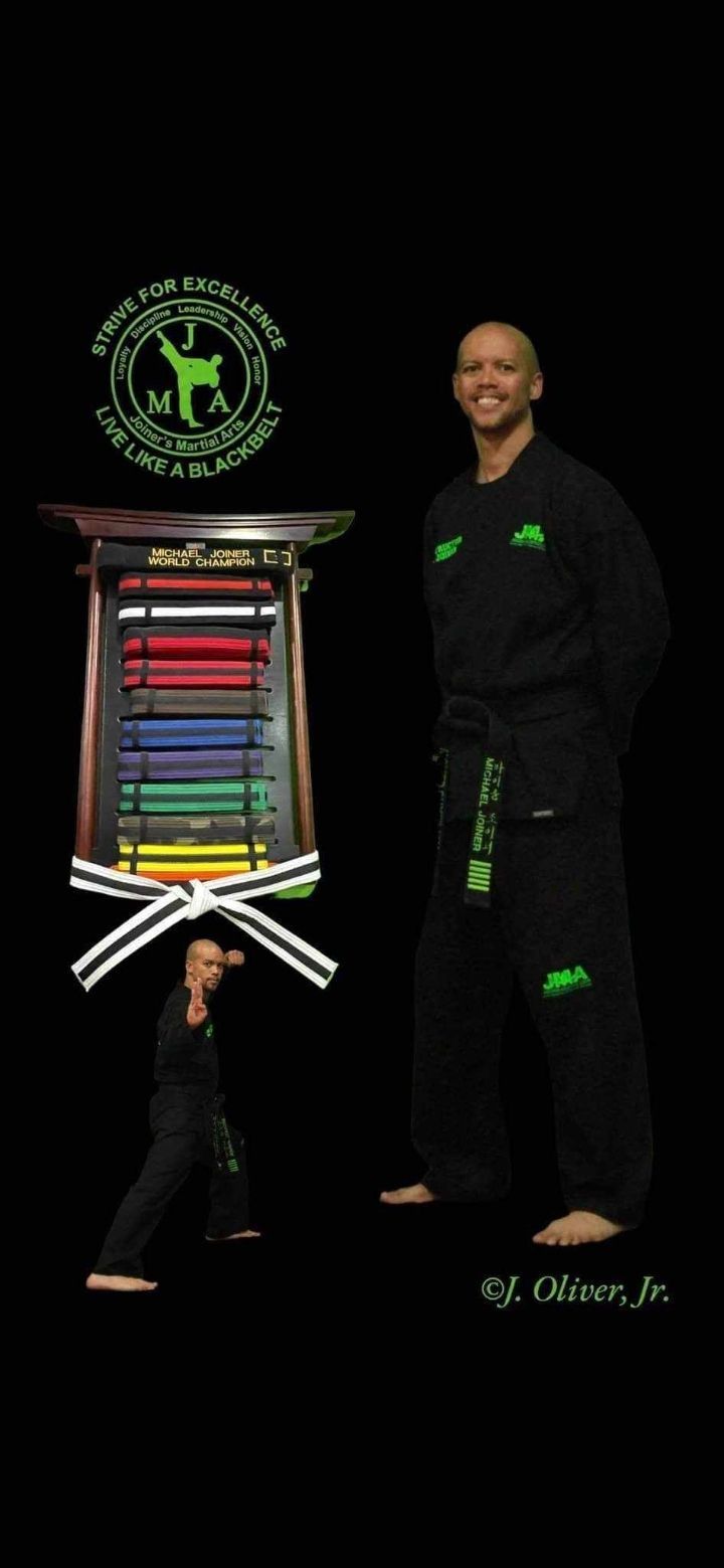 Martial artist in black uniform, smiling, beside a belt display, black background.