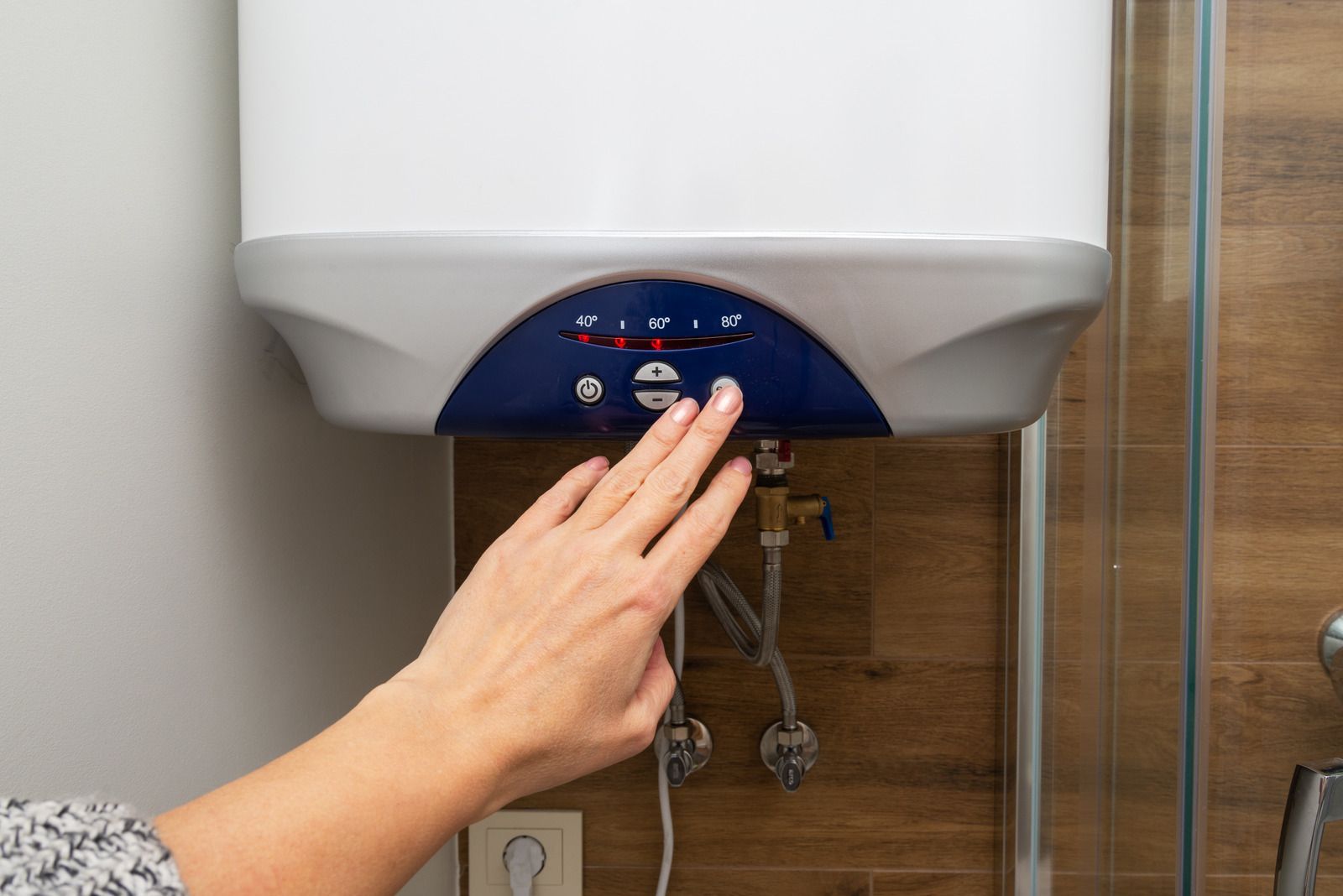 Hand adjusting controls on a white water heater above a sink