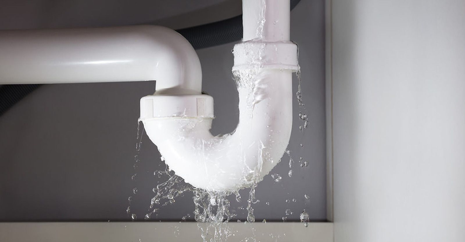 White plumbing pipes leaking water against a white wall.