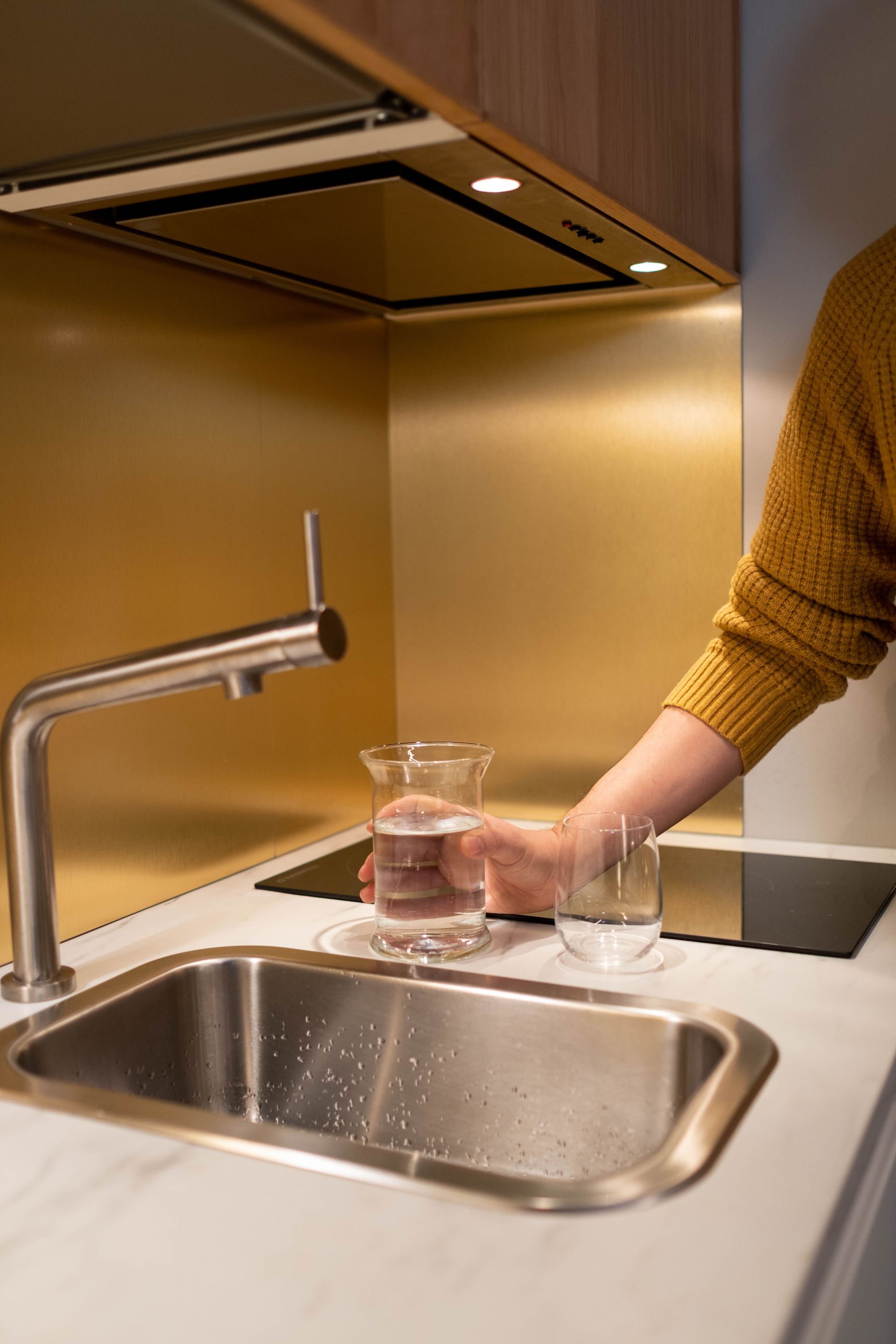 Hand rinsing a glass under a kitchen faucet over a stainless-steel sink.