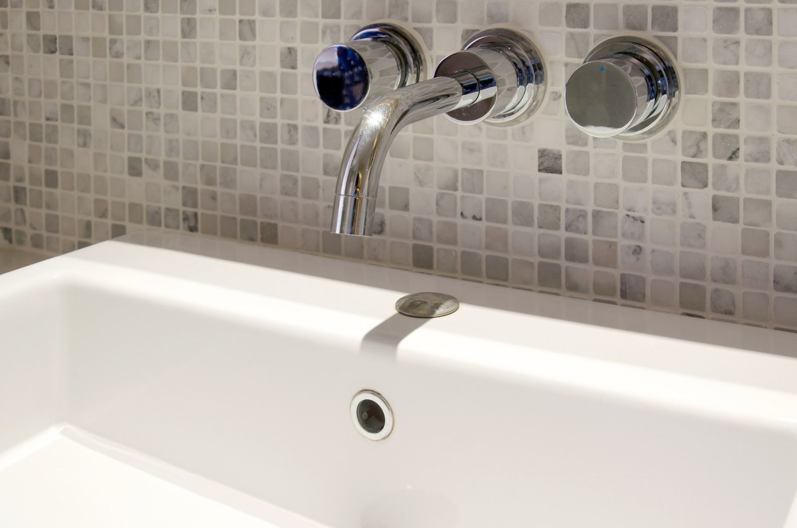 Modern white bathtub with chrome faucet and tiled backsplash.