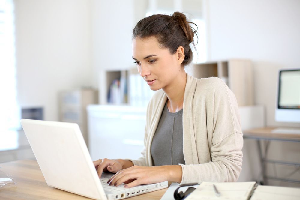 A Woman Is Sitting At A Desk Using A Laptop Computer — Black Label I.T. in Garbutt, QLD
