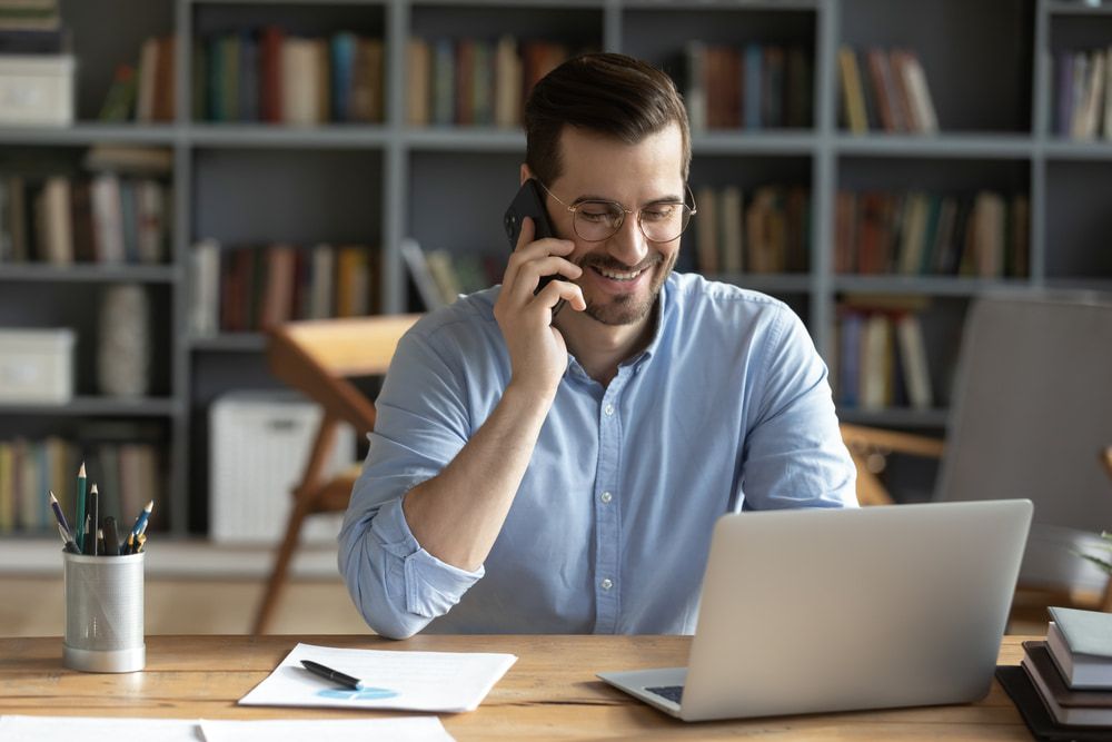A Man Is Sitting At A Desk With A Laptop And Talking On A Cell Phone — Black Label I.T. in Garbutt, QLD