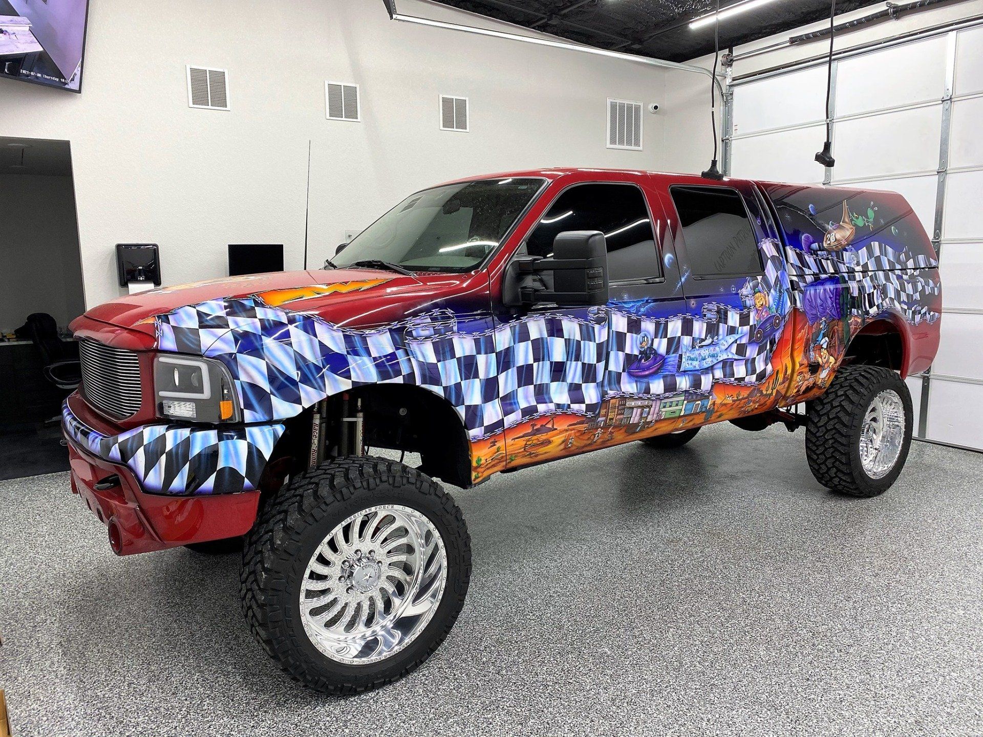 A red truck with a checkered wrap is parked in a garage.