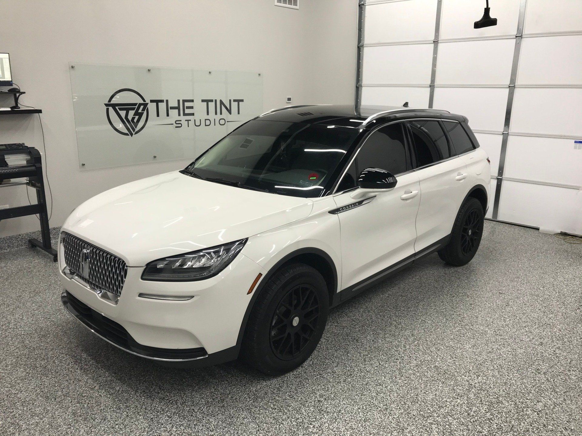 A white car is parked in a garage next to a sign that says the tint studio.