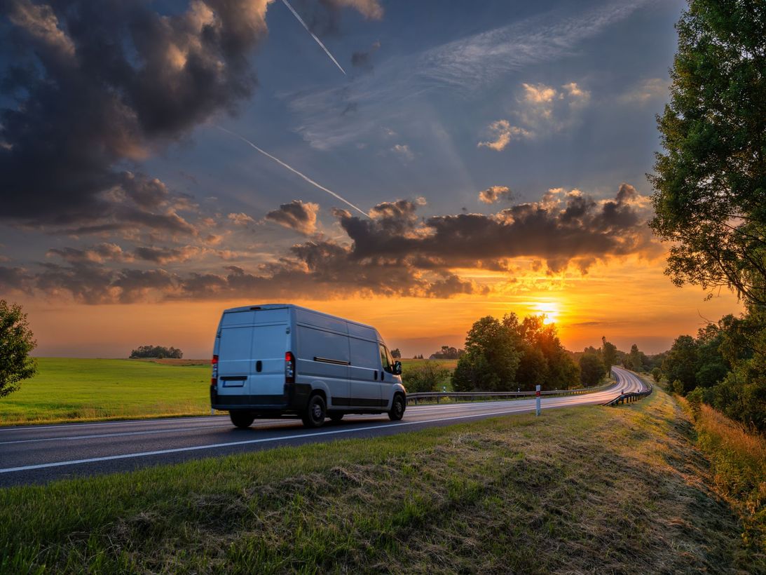 White van driving on a rural road at sunset under dramatic clouds