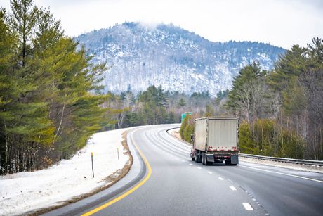 Truck driving on a snowy mountain highway with trees and hills in the background