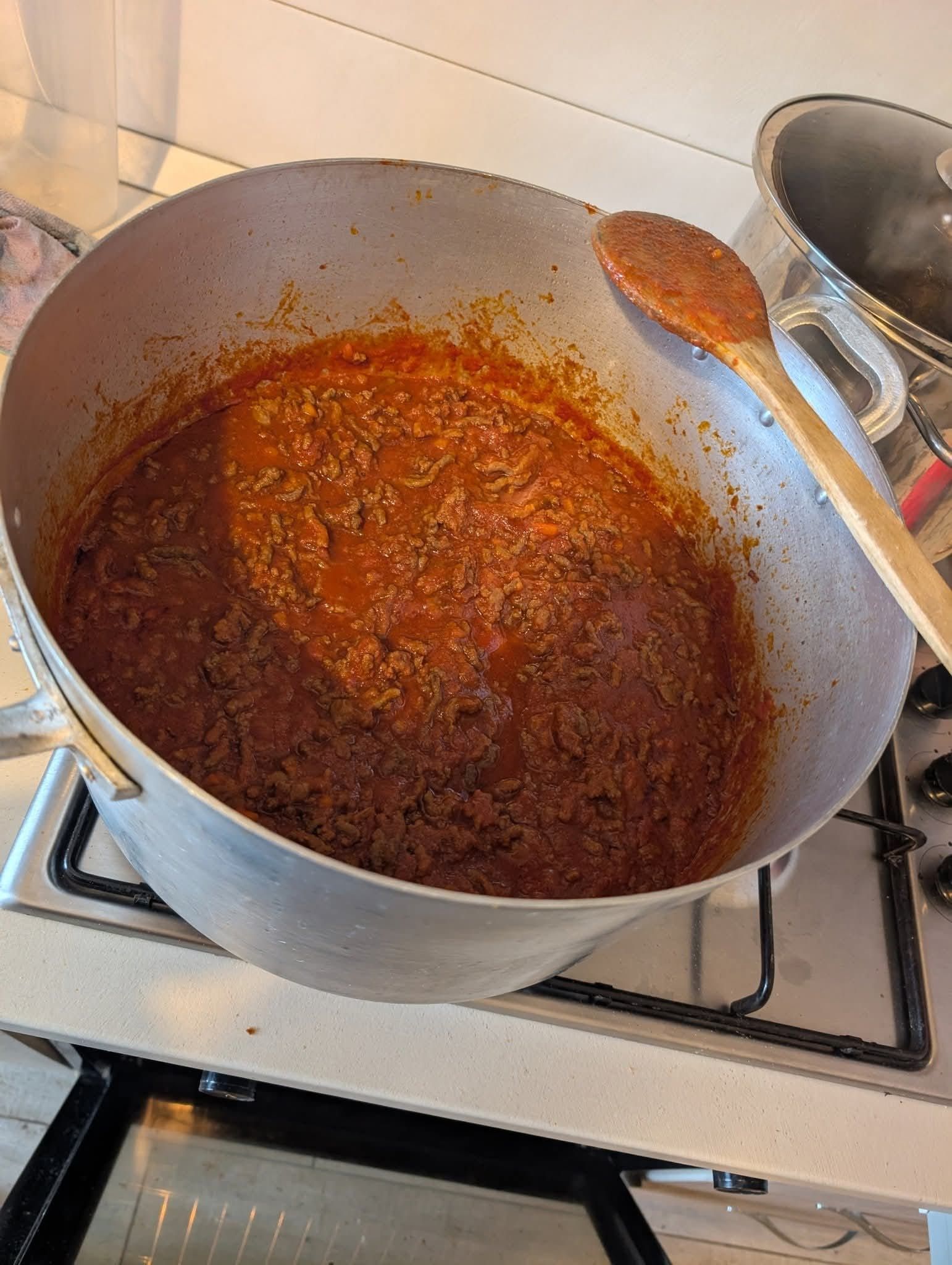 Una grande pentola d'argento sul fornello, contenente una densa salsa rossa a base di carne, con un cucchiaio di legno appoggiato all'interno.