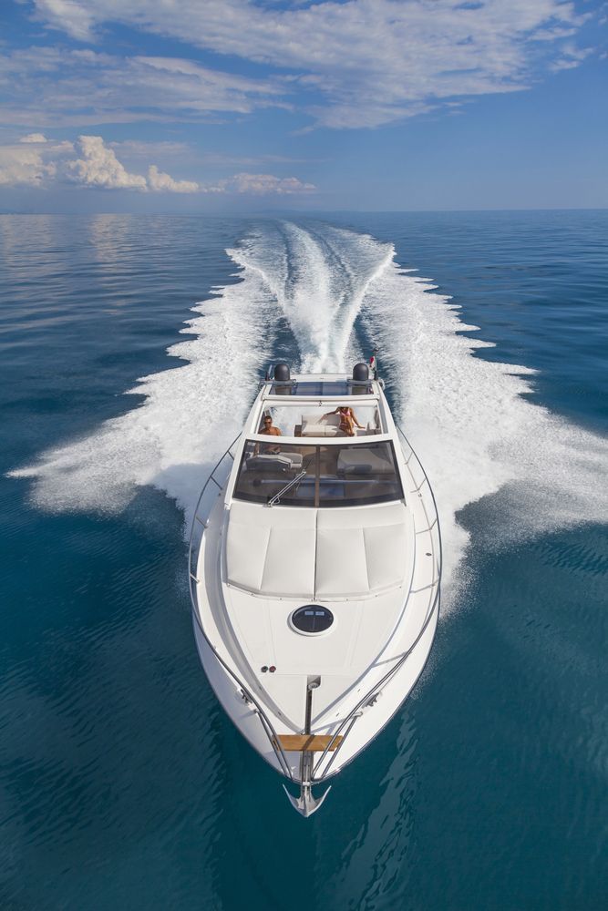 Un motoscafo bianco sfreccia sull'acqua blu, creando scie bianche. Giornata di sole.