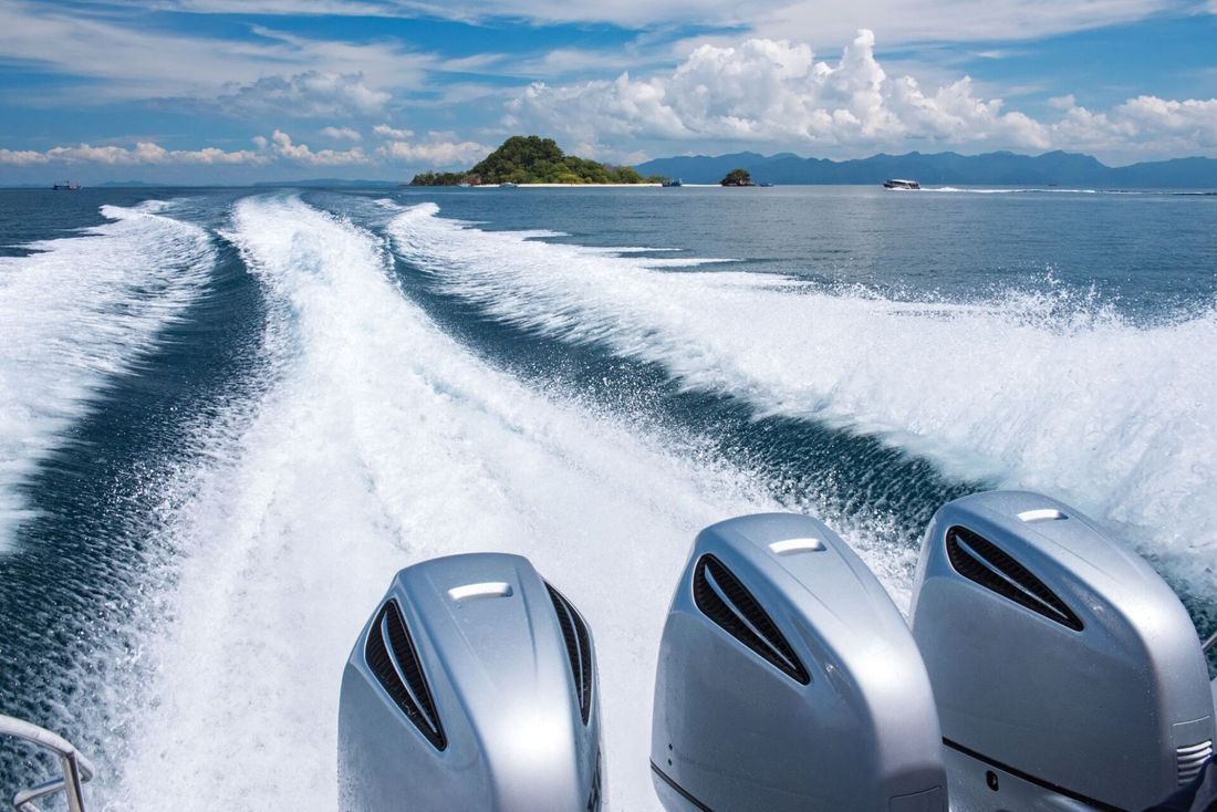 Tre motori di barche creano scie bianche nell'oceano blu, con un'isola in lontananza.