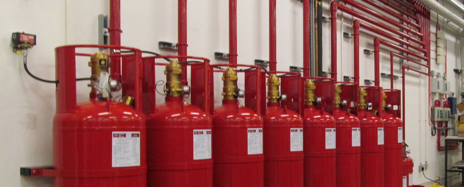 A row of red gas cylinders are lined up on a wall.