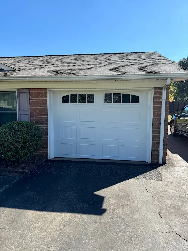 Suburban house exterior with white garage door, brick siding, and driveway in sunlight