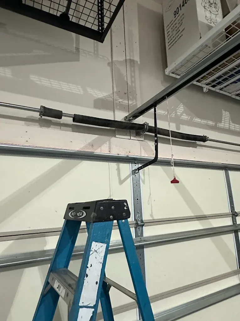 Blue ladder in a garage beside an overhead garage door and ceiling-mounted tracks.