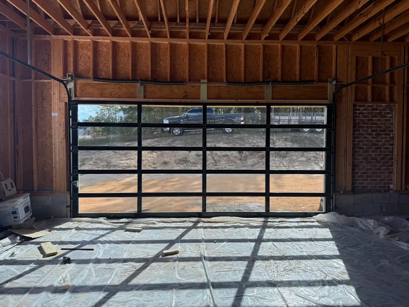 Empty garage with a large glass-paneled overhead door and sunlight casting shadows on the concrete floor