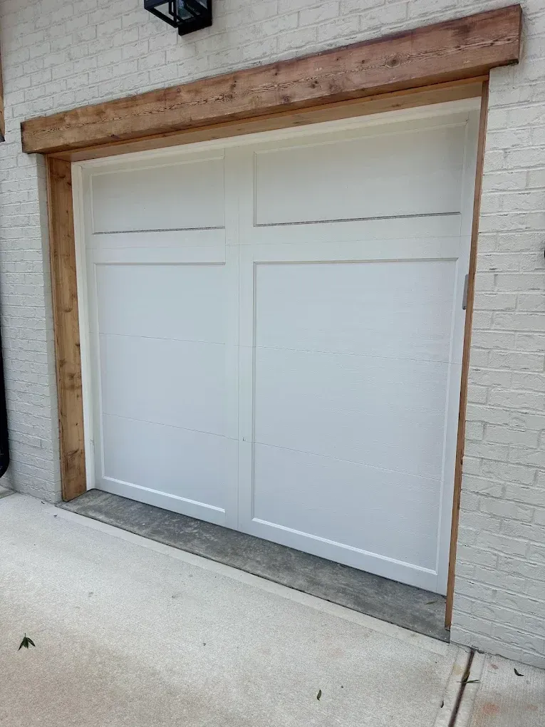 White garage door with small windows, set in a brick wall beneath a wooden beam.