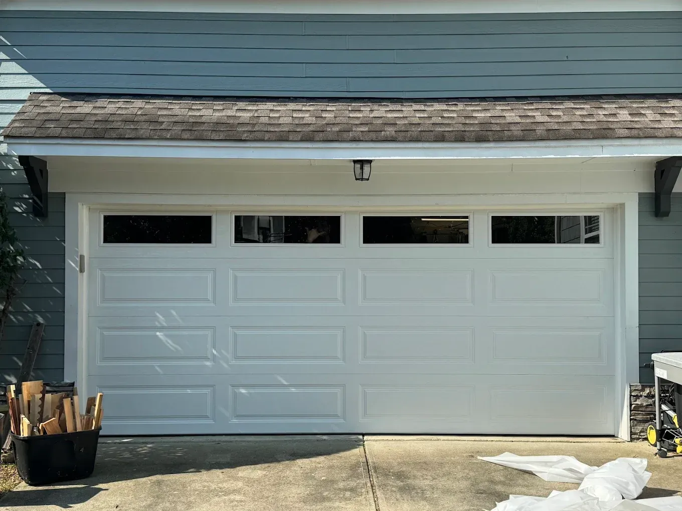 White double garage door on a house exterior with small windows and a shingled roofline.