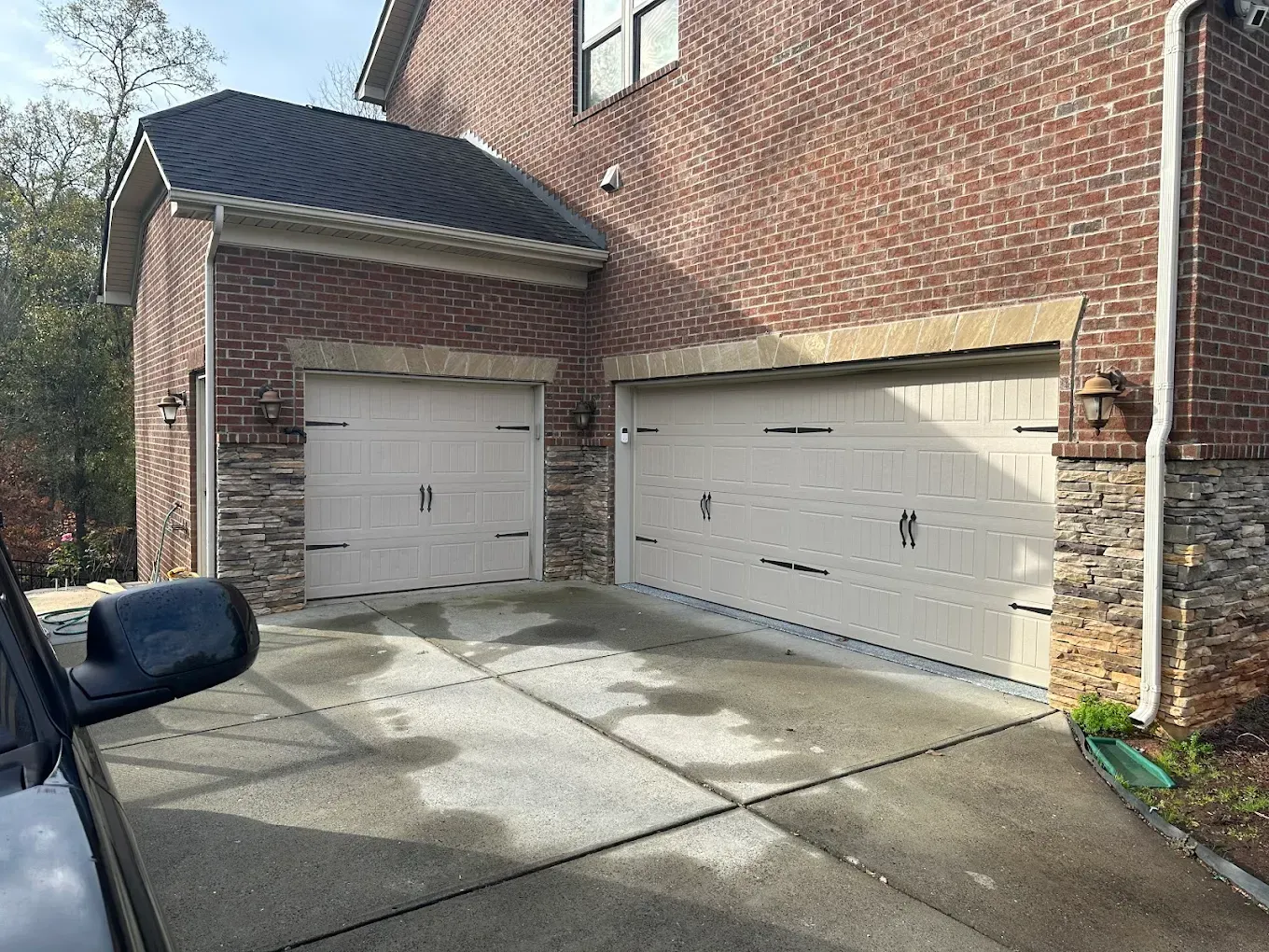 Brick house with two white garage doors and a concrete driveway in daylight
