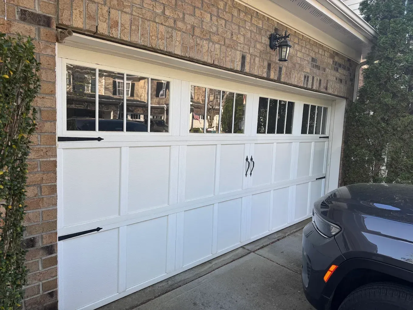 White garage door with windows on a brick house, with a dark SUV parked beside it.