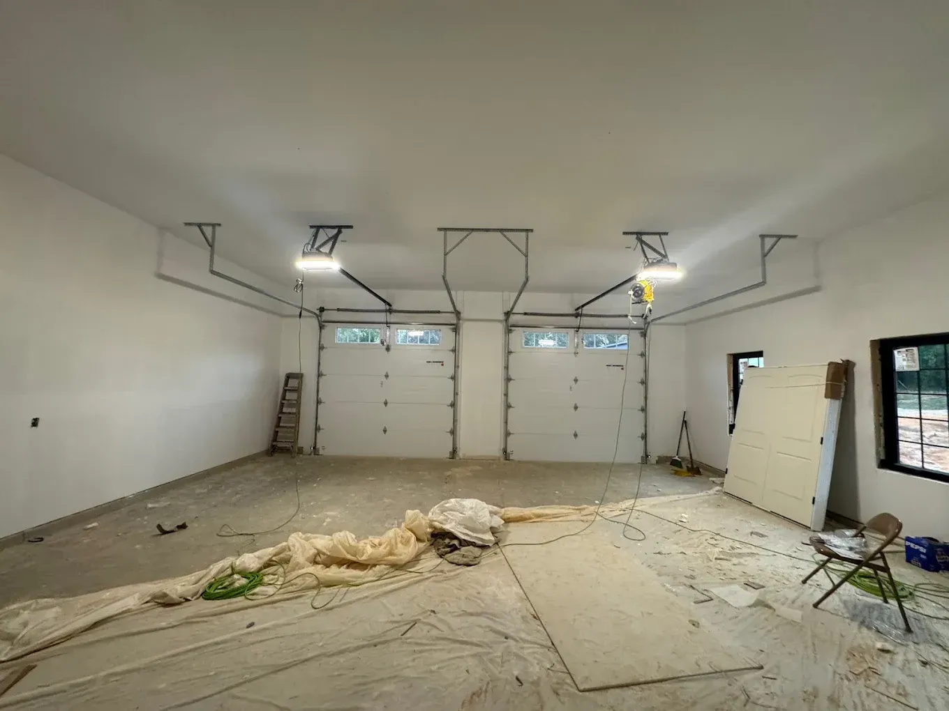 Unfinished garage interior with drywall, exposed ceiling fixtures, and construction debris on the floor