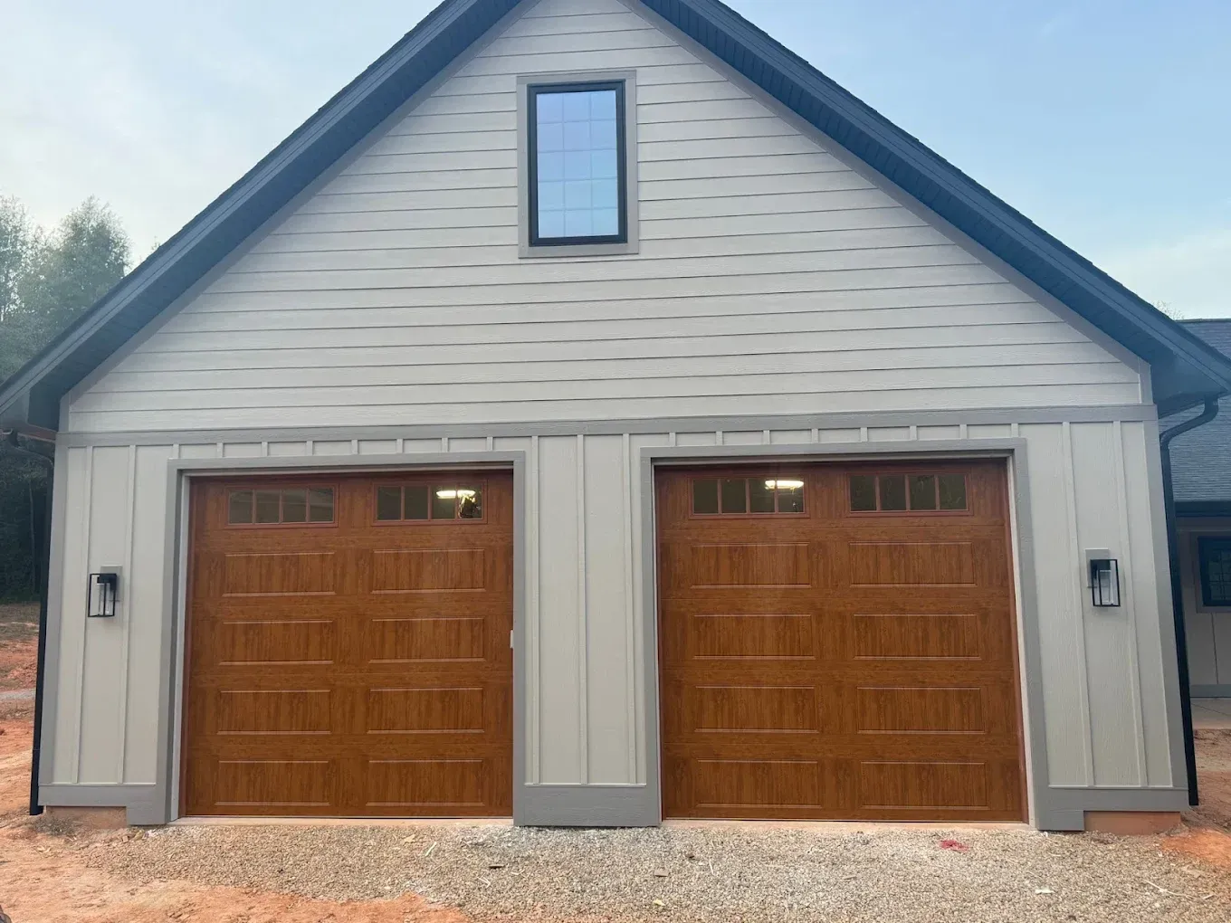 Two-car detached garage with gray siding and brown wooden doors, plus a small upper window.